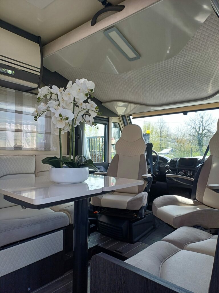 Intérieur d’un camping-car CI 67 intégral avec une table centrale et des sièges capitonnés autour, accompagné d'une décoration florale.