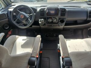 Driving position of a CI 67 Magi integral motorhome with a Fiat dashboard, ergonomic steering wheel and upholstered front seats.