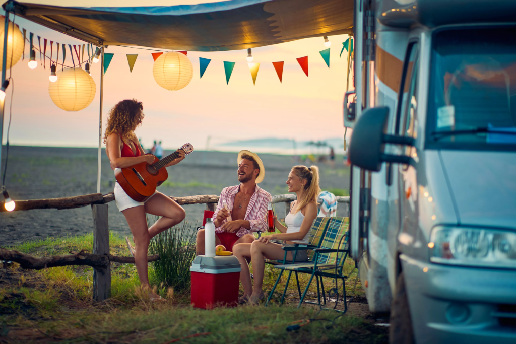 three people enjoying a relaxing moment at a campsite near a beach, next to a camper van